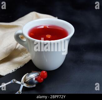 Heißen Tee aus einem viburnum in eine weiße Keramik Tasse auf einem schwarzen Hintergrund Stockfoto