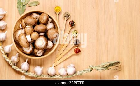 Pilze in Holzplatte, Zopf aus Knoblauch, Lorbeerblättern, mehrere kleine Löffel mit verschiedenen Gewürzen. Draufsicht. Stockfoto