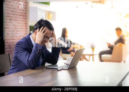 Portrait von Asiatische Geschäftsmann Belastung und erhielt unter Druck Nach siehe Daten im Smartphone und Laptop und nicht für seine Arbeit im Cafe mit Business Team in Ba Stockfoto