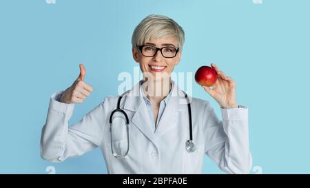 Richtige Ernährung Konzert. Frau Arzt Gestik Zeichen ausgezeichnet und hält Apfel Stockfoto