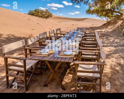 Ein langer Holztisch und Stühle für ein touristisches Mittagessen in der Sahara, Marokko vorbereitet. Konzeptionell für Last-Minute-Touristen und Reiseabsagen Stockfoto