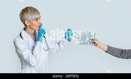 Frau Ärztin in medizinischen Handschuhen nimmt Geld von den Händen des Patienten und macht Zeichen der Stille Stockfoto