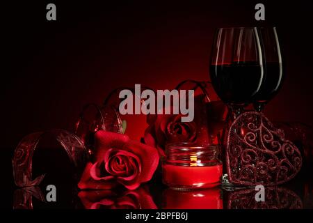 Stillleben mit Rosen, roten Herzen und zwei Gläsern Wein auf rotem Hintergrund. Valentinskarte mit Kopierfläche. Design-Element für romantische gre Stockfoto