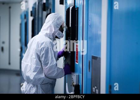 Ein Mitglied des PSNI Musgrave Street Custody Teams schaut durch eine Zellentür mit der PPE, die für die Interaktion mit einer mutmaßlichen Covid-19-Person in einem Gefangenenblock auf der Station in Belfast erforderlich ist. PA Media erhielt exklusiven ersten Zugang zum Covid-19 Block, um zu sehen, wie sich der Polizeidienst von Nordirland (PSNI) an die Herausforderungen der Haft in einer Pandemie angepasst hat. Stockfoto