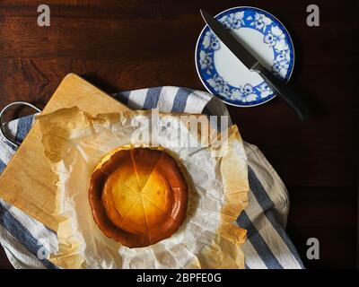 Draufsicht des baskischen gebrannten Käsekuchen und Messer auf einem Teller auf Holztisch. Stockfoto