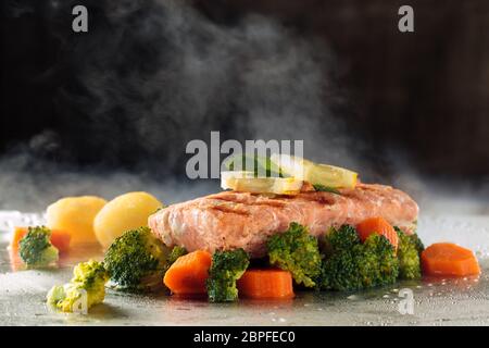 Lachssteak und gedünstetem Gemüse auf Tray mit Dampf. Stockfoto