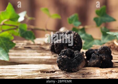 Schwarze Trüffeln und Blätter auf alten Holztisch. Stockfoto