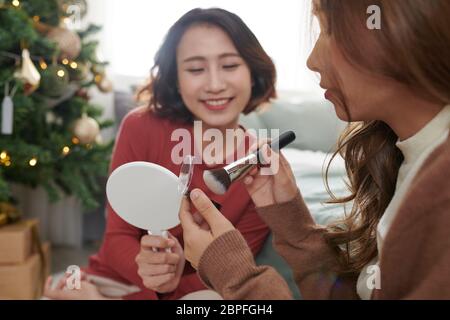 Kreative junge Frau, die Make-up auf das Gesicht eines Freundes im Wohnzimmer aufführt Stockfoto