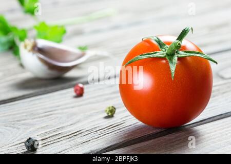 Eine reife Kirschtomate, eine Knoblauchzehe, Grüns und ein paar Pfefferkörner auf einer Holzfläche. Stockfoto