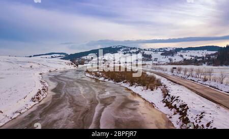 Gefrorene winter River. Antenne Blick auf verschneite Dorf und auf der Straße. Schmelzender Schnee und Eis im frühen Frühling. Stockfoto