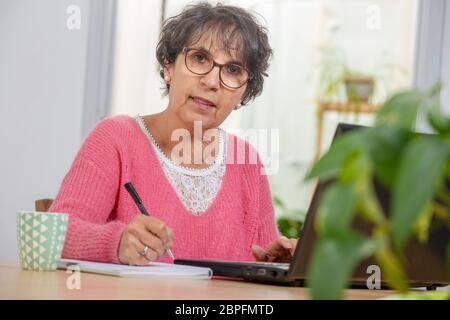 Schöne Brünette reife Frau in Rosa mit einem Laptop zu Hause angezogen Stockfoto