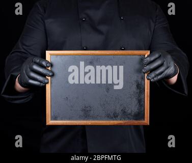 Koch in schwarzer Uniform und schwarzem Latex Handschuhe hält einen leeren Rahmen aus Holz, ein leerer Raum Stockfoto