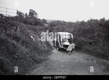 1950er Jahre, historisch, eine Dame, die am offenen Kofferraum steht, hinter ihrem Wagen, möglicherweise ein Ford Anglia, ein beliebtes Auto in dieser Zeit, geparkt auf einer schmalen, holprigen Landstraße, umgeben von dicken, hohen Hecken, England, Großbritannien. Stockfoto