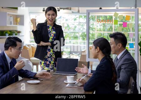 Portrait von Vertrauen asiatischen Geschäftsfrau froh, mit ihr zu arbeiten stehen vor der Tabelle im Tagungsraum des Cafe mit Business Team im Hintergrund Ig Stockfoto
