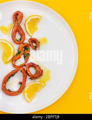 Frischer Tintenfisch Grill mit Zitrone geschnitten, Calamari Ringe auf weißem Teller auf gelbem Hintergrund. Selektiver Fokus. Draufsicht Stockfoto