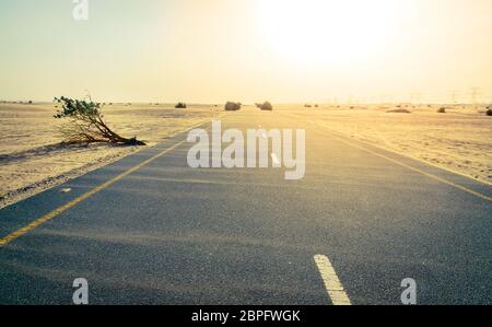 Sand weht über einer Wüste Straße in der Nähe von Dubai in den Vereinigten Arabischen Emiraten. Stockfoto