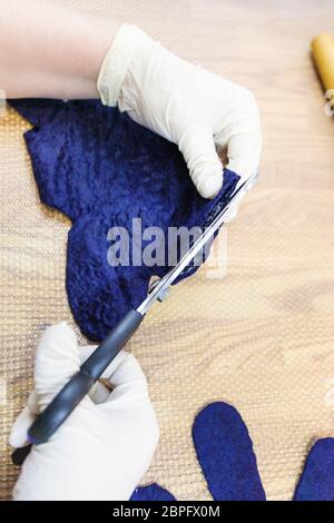 Werkstatt von Hand eine Fleece Handschuhe von blau Merino Schafschurwolle nass Filzen Prozess - Handwerker schneidet die Kante in die gefilzte Handschuh nach Rollen Stockfoto