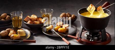 Panorama Banner der Käsefondue und Seiten mit zwei Gabeln mit geröstetem Brot in die Sauce in einen gusseisernen Topf auf einem Brenner eingetaucht werden Stockfoto