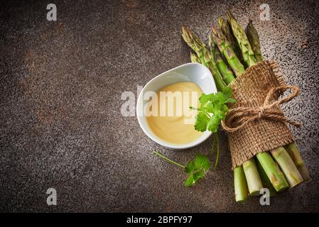 Bündel von frischem grünen Spargel gefesselt und mit einem Sack eingerichtet, serviert mit cremigen Soße in Weiß bawl, von oben mit Kopie Raum gesehen auf dunklen Stockfoto