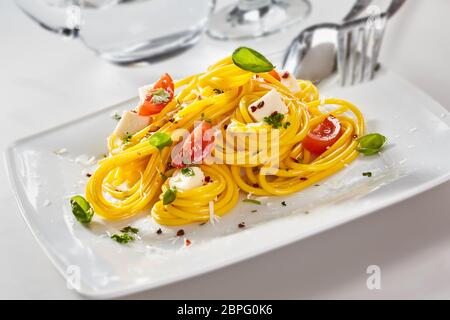 Italienische Spaghetti Nudeln mit Feta Käse, Keile mit frischen Tomaten und Basilikum auf einem rechteckigen weißen Teller Stockfoto