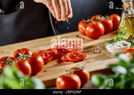 Hand eines Kochs würzen geschnittene Tomaten auf einer hölzernen Schneidebrett in der Nähe zu sehen. Stockfoto