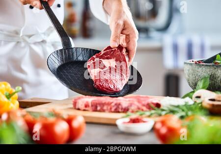 Koch einen dicken Ausschreibung raw Rumpsteak in einer Pfanne bereit für das Kochen in einem Restaurant mit frischen Zutaten in Nahaufnahme auf seinen Händen umgeben Stockfoto