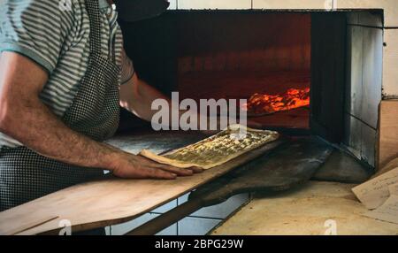 Türkisch-muslimischer Bäckerkoch, der traditionelles ramadan-Brot der türkischen Küche in den Ofen stellt, in den heiligsten Monaten des muslims Stockfoto