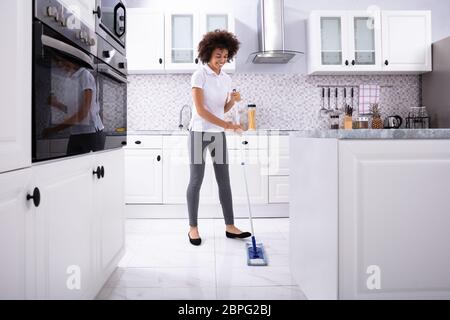 Seitenansicht eines Lächelnd weibliche Hausmeister Reinigung weißen Boden mit Mop In der Küche Stockfoto