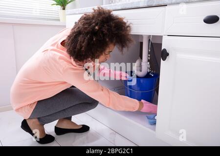 Nahaufnahme einer jungen Frau die blauen Eimer unter Wasser leckt von der Spüle Leitung Stockfoto