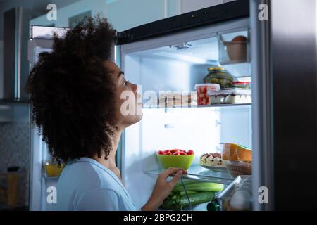 Seitenansicht der jungen afrikanischen Frau Suche Essen in einem offenen Kühlschrank Stockfoto
