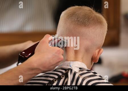 Frisur, Friseursalon für Herren. Nahaufnahme von Mann Hände Pflege Kind Jungen Haare im Friseur. Junge Schnitt mit Friseur Stockfoto