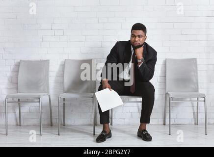 Junger schwarzer Mann fühlt sich erschöpft vom Warten auf sein Vorstellungsgespräch im Bürogebäude. Leerer Speicherplatz Stockfoto