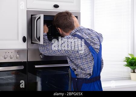 Seitenansicht des jungen Mannes Instandsetzung Mikrowelle Ofen in der Küche Stockfoto