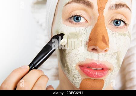 Schönheitsbehandlungen Hautpflege. Junge Frau mit Gesicht grau und rot Schlamm Clay Mask zu ihrem Gesicht im Badezimmer. Frau mit verschiedenen Masken auf Ihrem Stockfoto