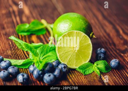 Frische Heidelbeeren, die Hälfte der Limette und Minze auf hölzernen Tisch. Zutaten für die Vorbereitung infundiert Wasser. Stockfoto