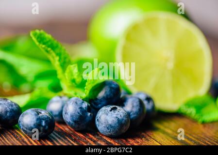 Frische Heidelbeeren und die Hälfte der Limette und Minze auf Hintergrund. Zutaten für die Vorbereitung der Reinigung Wasser. Stockfoto