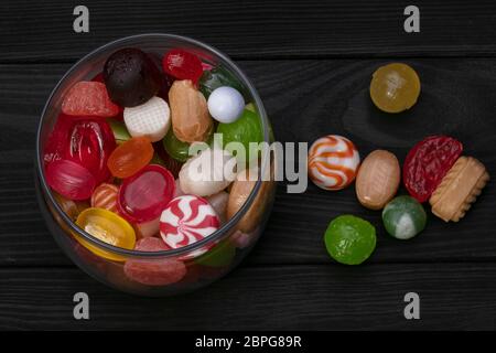 Süßigkeiten in einem Glas auf dunklem Hintergrund. Mehrfarbiges Karamell auf einem Holzbrett. Süßigkeiten. Stockfoto