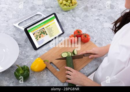 Frau Schneiden Gurken mit Messer in der Nähe Rezepte Kochen auf digitalen Tablet Bildschirm Stockfoto