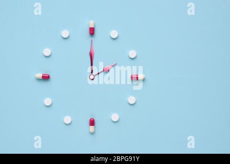 Uhr aus Pillen und Kapseln auf pastellblauem Hintergrund erstellt. Richtige Zeit für die Verwendung von Medikamenten. Flaches Lay. Stockfoto