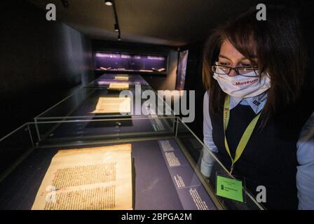 19. Mai 2020, Rheinland-Pfalz, Mainz: Eine Mitarbeiterin mit Gesichtsmaske betrachtet eine typische Handschrift aus der Zeit vor der Erfindung des Buchdruckdrucks in der Schatzkammer des Museums. Das Gutenberg-Museum öffnet ab heute wieder seine Pforten für Besucher. Aufgrund der Corona-Pandemie war das Museum seit Anfang März geschlossen. Foto: Andreas Arnold/dpa Stockfoto