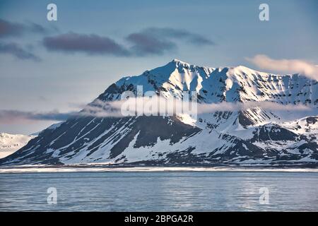 Bergszene mit schneebedeckten Gipfeln, die in Wolken bei Spitzbergen, Svalbard, Nordnorwegen, umraht sind Stockfoto