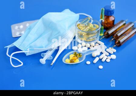 Medizinische Schutzmaske mit Pillen, Thermometer, Medikamente, Spritzen auf blauem Schreibtisch. Gesundheitskonzept und medizinisches Konzept. Stockfoto