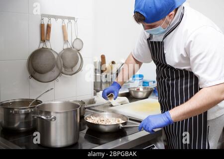 Mann in Maske und Handschuhe, Gewürze zu frischen Pilzen hinzufügen Stockfoto