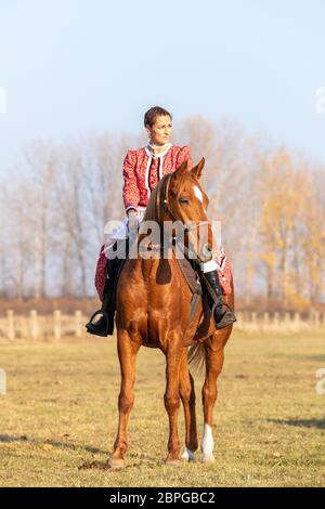 HORTOBAGY, UNGARN, NOVEMBER 04. 2018: Ungarische Csikos-Frau in traditioneller Tracht auf ihrem trainierten Pferd. November 04. 2018, Hortobagy, Hun Stockfoto