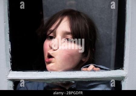 11-jähriger Junge, der während des Schließens gegen die Fensterscheibe macht. Stockfoto