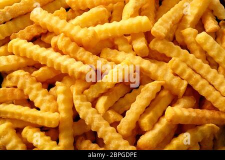 Nahaufnahme Hintergrund der Crinkle cut knusprige Golden fried Potato Chips, Pommes frites, Pommes Frites Inn a full frame anzeigen Stockfoto