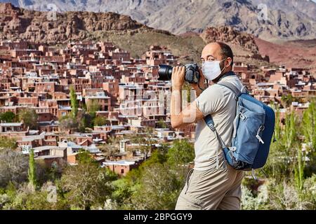 Kaukasischer Reisender in einer Einweg-Schutzmaske als Schutz während der Coronavirus-Pandemie-Infektion covid-19 ist die Aufnahme von Fotos in Abyaneh Stockfoto