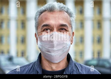 Lächelnder weißer kaukasischer Mann in einer Einweg-Schutzmaske in einer Periode des Coronavirus Covid-19 Pandemie geht auf der Straße. Stockfoto