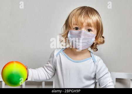 Kleine weiße kaukasische Mädchen etwa 3 Jahre alt in Einweg-Schutz Gesichtsmaske medizinische Maske spielt mit Ball auf zu Hause Isolation während covid-19 pand Stockfoto