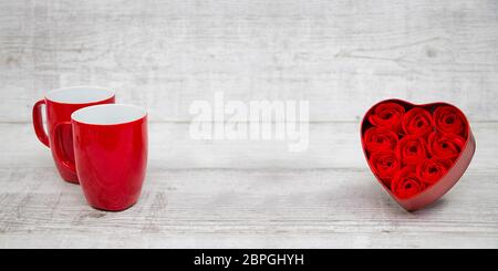 Glänzende rote Kaffeetassen und rote Herzrosen Stockfoto